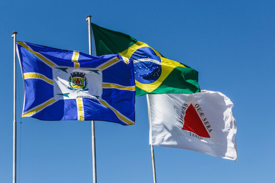 Official flags of the country brazil, state of minas gerais and city of araguari. Swaying in the wind under the blue sky.