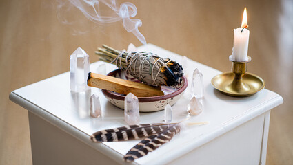 A calming atmosphere is created with sage burning, surrounded by clear crystals and a lit candle on a white table. The setting suggests a spiritual practice for well-being.