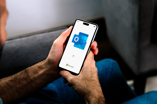 Man holding a mobile phone opening Outlook app for email of Microsoft. ROSARIO, ARGENTINA - APRIL 30, 2025.