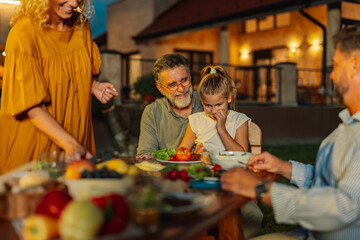 Family enjoying evening meal together in backyard of house