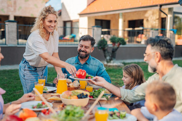Happy family enjoying backyard meal together, serving fresh vegetables