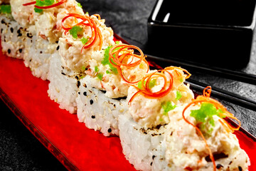 Delicious uramaki sushi rolls with cream cheese topping and tobiko on red plate