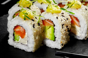 Uramaki sushi rolls with salmon, avocado, cream cheese and sesame seeds on black background
