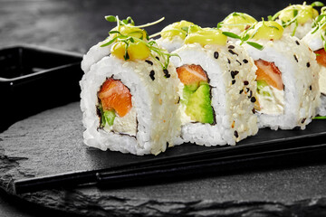 Delicious uramaki sushi rolls with salmon, avocado, cream cheese and mango sauce on dark background