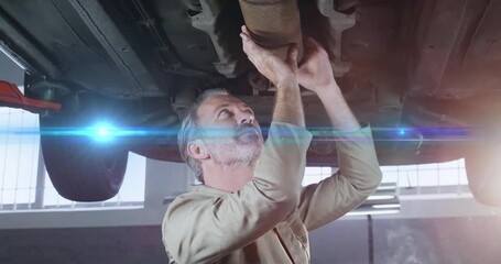 Senior mechanic inspecting exhaust pipe on lift in automotive garage, showing lens flare overlay