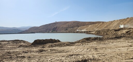 Construction Trucks Lined Up in a Rocky Quarry Near a Water Source in Algeria