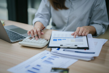 Young asian businesswoman holding pen and reading financial documents, smiling and working at office desk with computer showing graphs, startup business concept