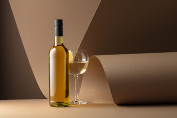 Bottle and glass of white wine on a beige background.
