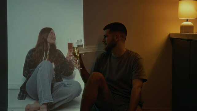 Full low key shot of young widower sitting by wall with glass of champagne and celebrating wedding anniversary with soul of deceased wife, missing his lost love