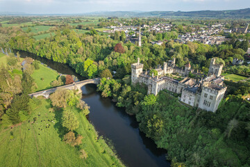  Aerial view of historic Lismore Castle and the surrounding townscape in County Waterford, Ireland, with lush spring greenery, the River Blackwater, and rolling countryside under soft evening light.