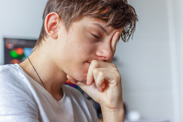 Portrait of a sad tired teenager, the guy supporting his face with his hand, thinking