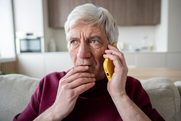 Suspicious stressed senior man frowns during unexpected call, listening to pressured demands for...