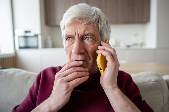 Suspicious stressed senior man frowns during unexpected call, listening to pressured demands for banking information. Fraud warning, social engineering pressure, personal data risk, financial scam
