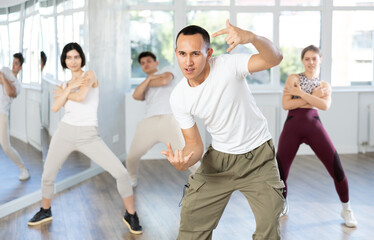 Cheerful young Asian man practicing modern street dancing during group class in choreographic studio..
