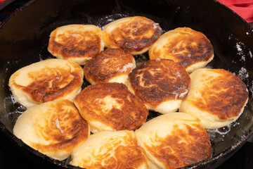 Golden brown pieces of fried dough sizzle in a black skillet, glistening with oil.