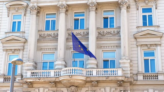 European union flag waving on building. European union flag gently waving on ornate balcony with classical architectural details, representing diplomatic significance of european governance