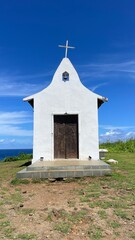 Saint Peter Chapel, a tiny whitewashed chapel built by fisherman on the top of a mound. Blue sky, white clouds, green lawn. Fernando de Noronha island, Brazil. Sunny day, beautiful view. Cirrus clouds