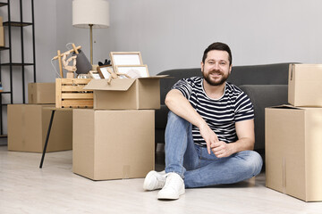 Moving day. Man resting on floor near cardboard boxes in his new home
