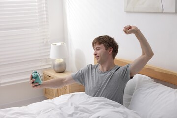Man with alarm clock stretching in bed indoors. Good morning