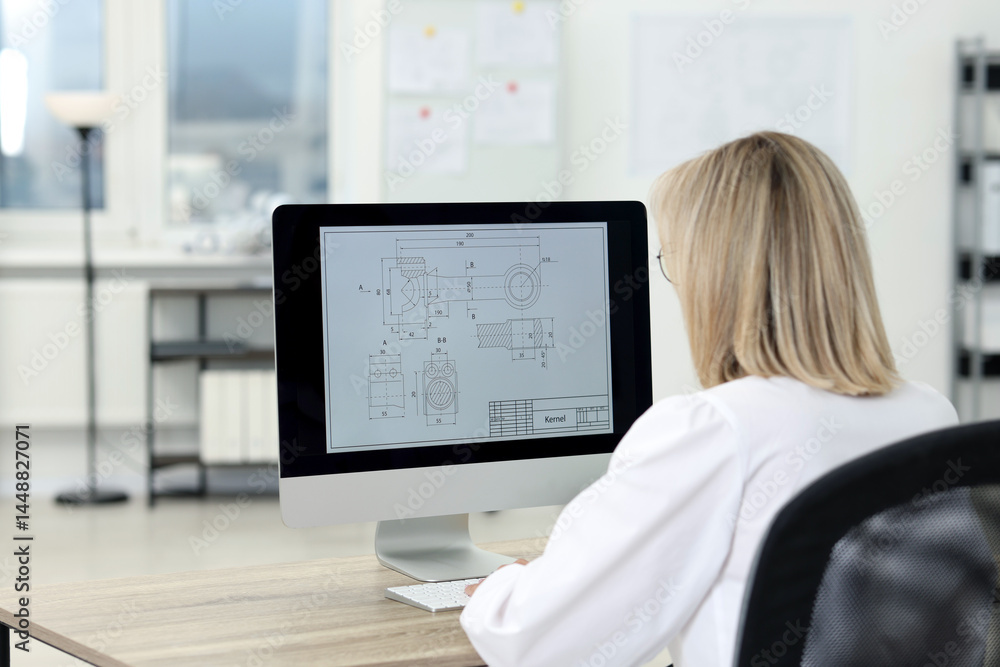 Poster technician making digital engineering drawing on computer at desk in office, back view