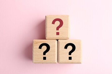 Wooden cubes with question marks on pink background, top view
