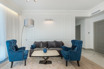 A bright living room with a gray sofa, turquoise armchairs and a small table on a gray carpet.