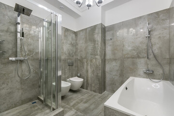 A modern bathroom decorated with gray marble tiles. Glass shower cabin with a tropical watering can.