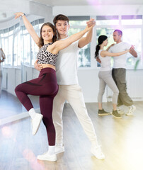 Happy young woman enjoying training dancing active swing with male partner in modern dance room....
