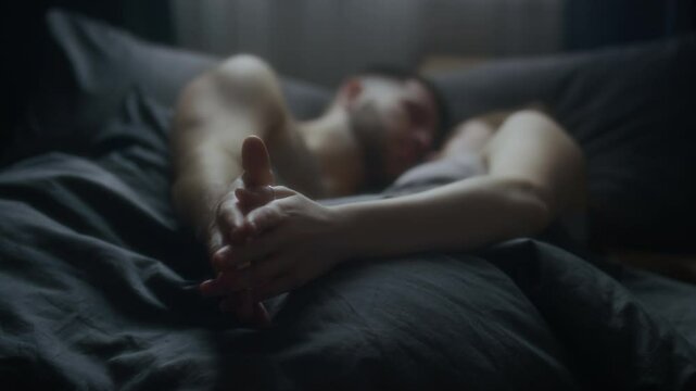 Close-up of young spouses intertwining fingers and holding hands while peacefully snuggling in bed after sleep in morning, deep love, affection and intimacy, focus of hands