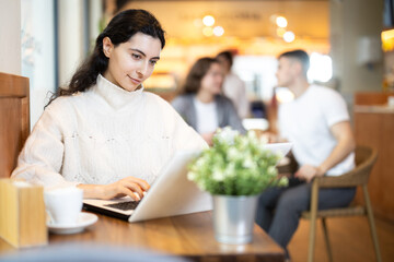 Young woman working on laptop drinking coffee in cafe