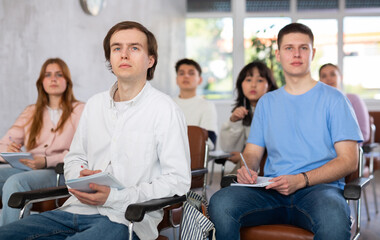 Interested concentrated guy student listening and taking notes of lecture while studying with...