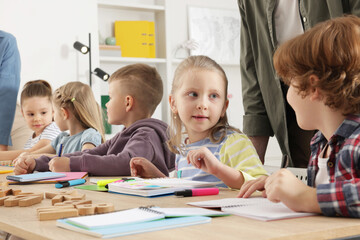 Children having lesson with teacher at desk indoors