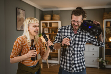 Adult couple sing karaoke on microphone and hold bottle of beer at home