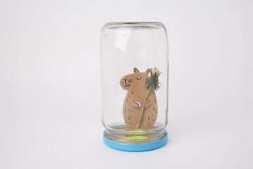 step in creative project Cute handmade capybara holding dandelion inside upside-down jar, ideal...