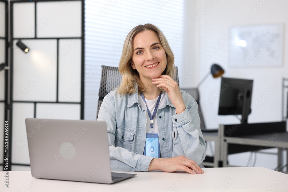 Poster smiling engineer working with laptop at table in office