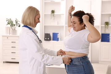 Happy woman lost weight. Smiling nutritionist measuring patient's waist with tape in clinic