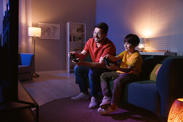 Happy father and his son playing video games on sofa in living room at night