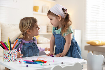 Cute little sisters drawing at white table in room