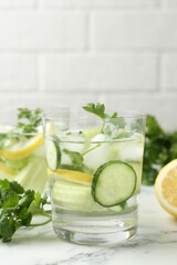 Healthy drink with parsley, cucumbers, lemon and celery on white marble table, closeup