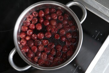Making compot of cherries. Simmering fruits in pot on stove, top view
