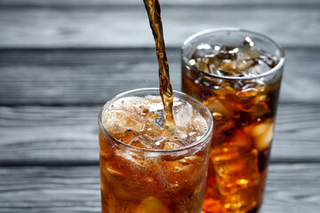 Pouring refreshing cola into glass at grey wooden table, closeup