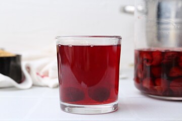Tasty cherry compot in glass on white tiled table, closeup