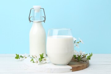Fresh milk and blossoms on white table against light blue background