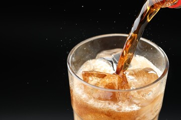 Pouring refreshing cola into glass on black background, closeup. Space for text