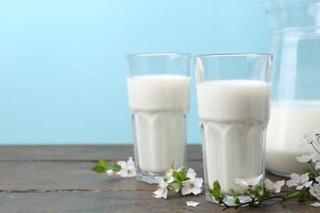 Fresh milk and blossoms on white table against light blue background. Space for text