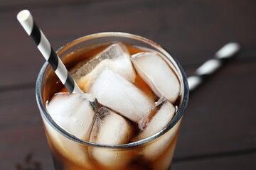 Refreshing cola with ice cubes and straw in glass on blurred background, closeup