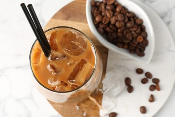 Tasty iced coffee and beans on white marble table, top view