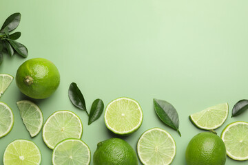 Fresh limes and leaves on pale green background, flat lay. Space for text