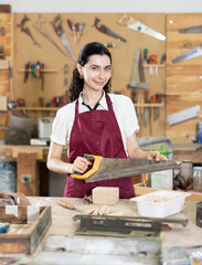 In carpentry workshop, girl master performs work, is engaged in production of wooden decorative...