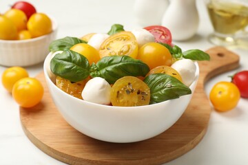 Fresh salad with yellow tomatoes, basil and mozzarella cheese on white table, closeup